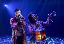 A Christmas Carol – review Paul Hilton (Ebenezer Scrooge) and Kibong Tanji (Ghost of Christmas Present) in A Christmas Carol at The Old Vic (2025). Photo by Manuel Harlan